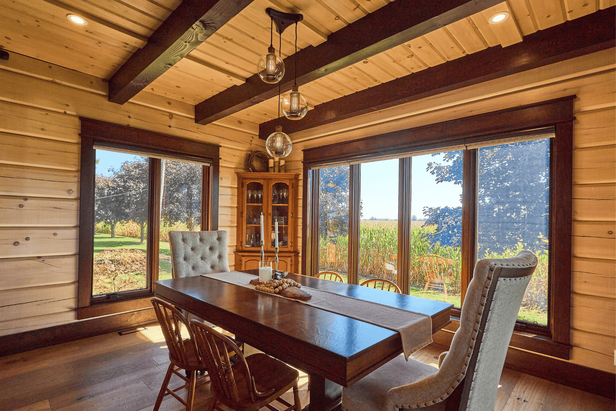 The dining of True North Log & Timber Homes’ award-winning Northern Escape. This dining room pairs the warmth of the timber trusses wooden window frames with whitewashed log wall and taupe decor.